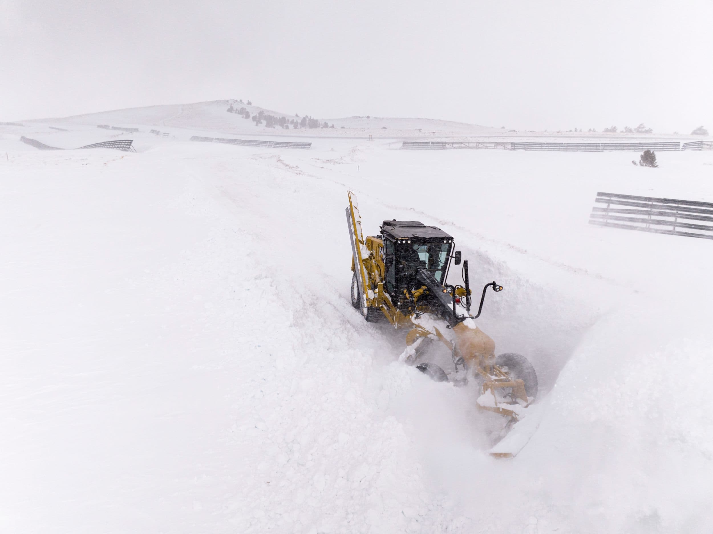 140 Motor Grader pushing snow in six-foot high snowdrifts. The machine has a snow wing in the upright position and a v-plow at the front moving the snow.
