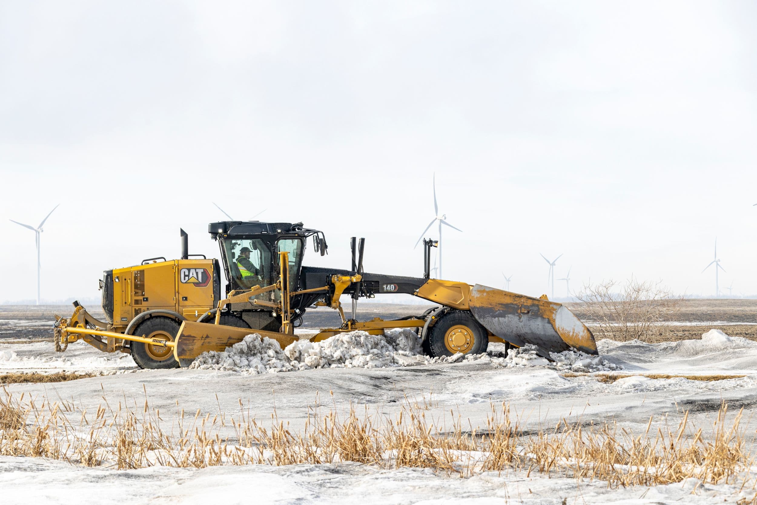 140 Motor Grader pushing snow with a snow wing on the side and a v-plow on front.